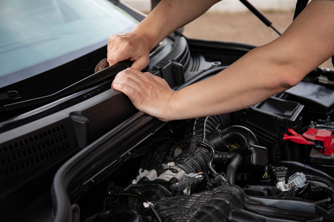 Close-up of hands repairing a car engine outdoors, focusing on automotive maintenance.